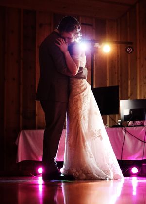 A couple's first dance silhouetted against pink and purple lighting in a rustic venue.