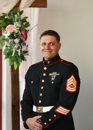 A Marine in dress blues uniform stands proudly in formal wedding attire.