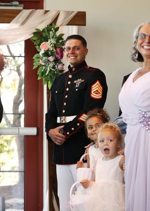 A small child in white reacts with surprise during a wedding ceremony.