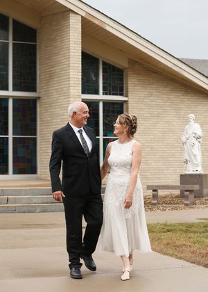 Bride and groom walking together outside a church, smiling at each other on their wedding day.