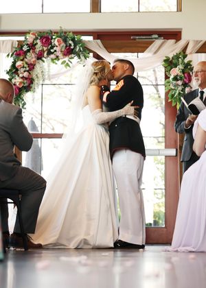A wedding ceremony in progress with floral decorations and white dresses.