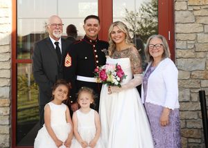 Wedding party poses together in formal attire with flower decorations.