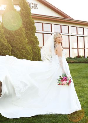 White wedding dress flows in breeze against green lawn and building backdrop.