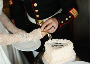 Close-up of hands cutting into an elegant white wedding cake with delicate details.