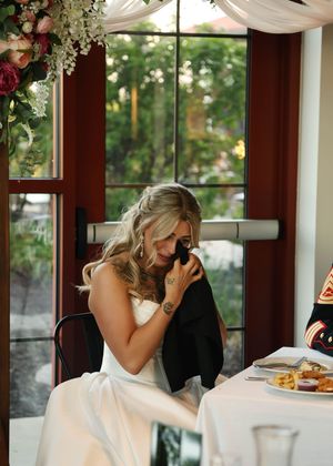 Romantic wedding reception scene with white drapes and floral decorations by large windows.