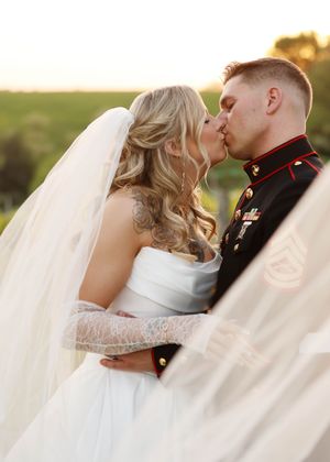 A romantic wedding moment captured during golden hour with flowing veil and military dress uniform.