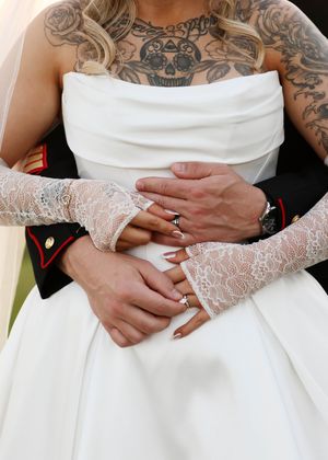 Close-up of tattooed arms and lace sleeves embracing during a wedding moment.