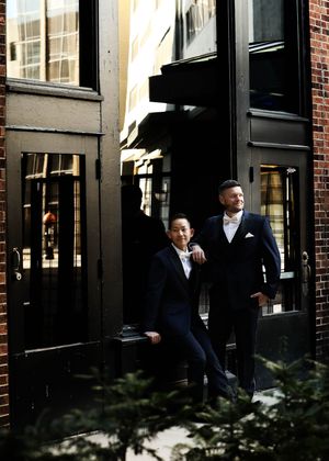 Groomsmen in navy suits stand outside a brick building before a wedding ceremony.