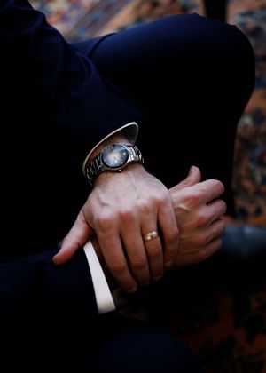 Detail shots of hands wearing wedding rings and watches against dark background.