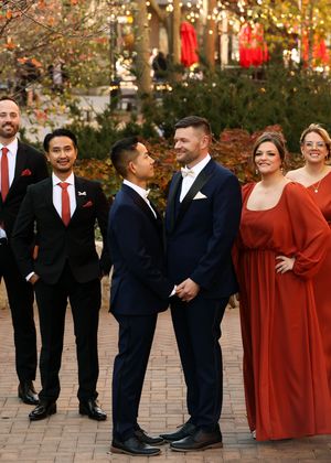 Wedding party in navy suits and burgundy dresses pose outdoors during autumn.