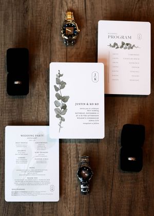 Wedding stationery and rings displayed on rustic wooden surface.