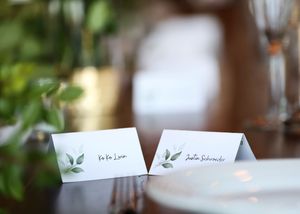 Two elegant place cards with leaf designs sit on a formal dining table setting.
