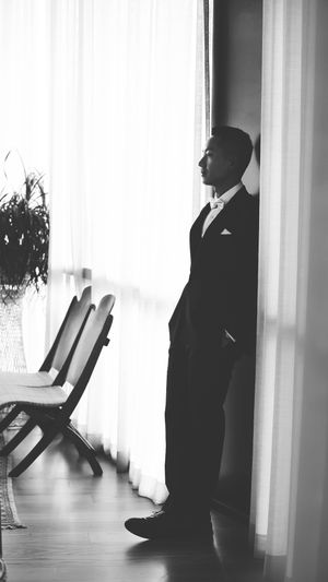 Silhouette of a person in formal attire standing by a window in black and white.