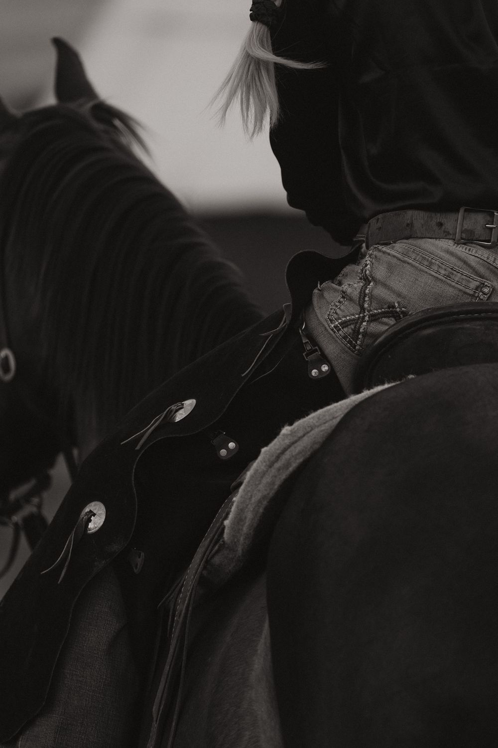Black and white close-up of a horse and rider showing saddle and riding equipment details.