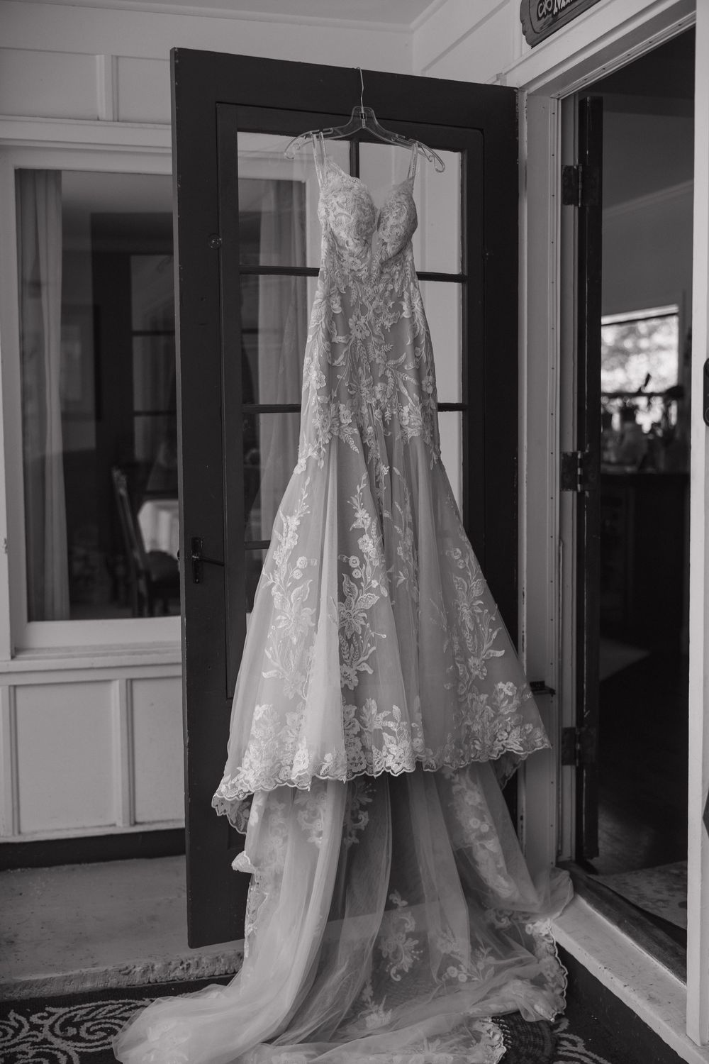 Wedding dresses displayed on hangers in elegant bridal boutique showroom with large windows and reflective lighting.