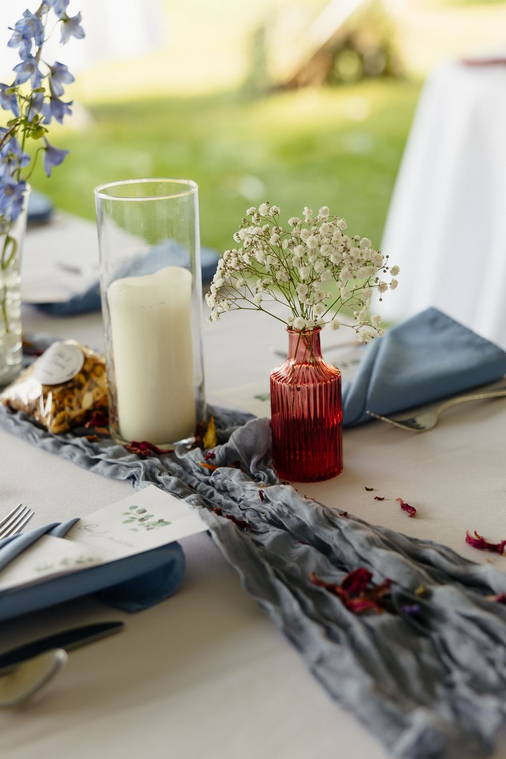 Detail shot of an elegant wedding table setting with gray linens, white candles, and delicate blue flowers.