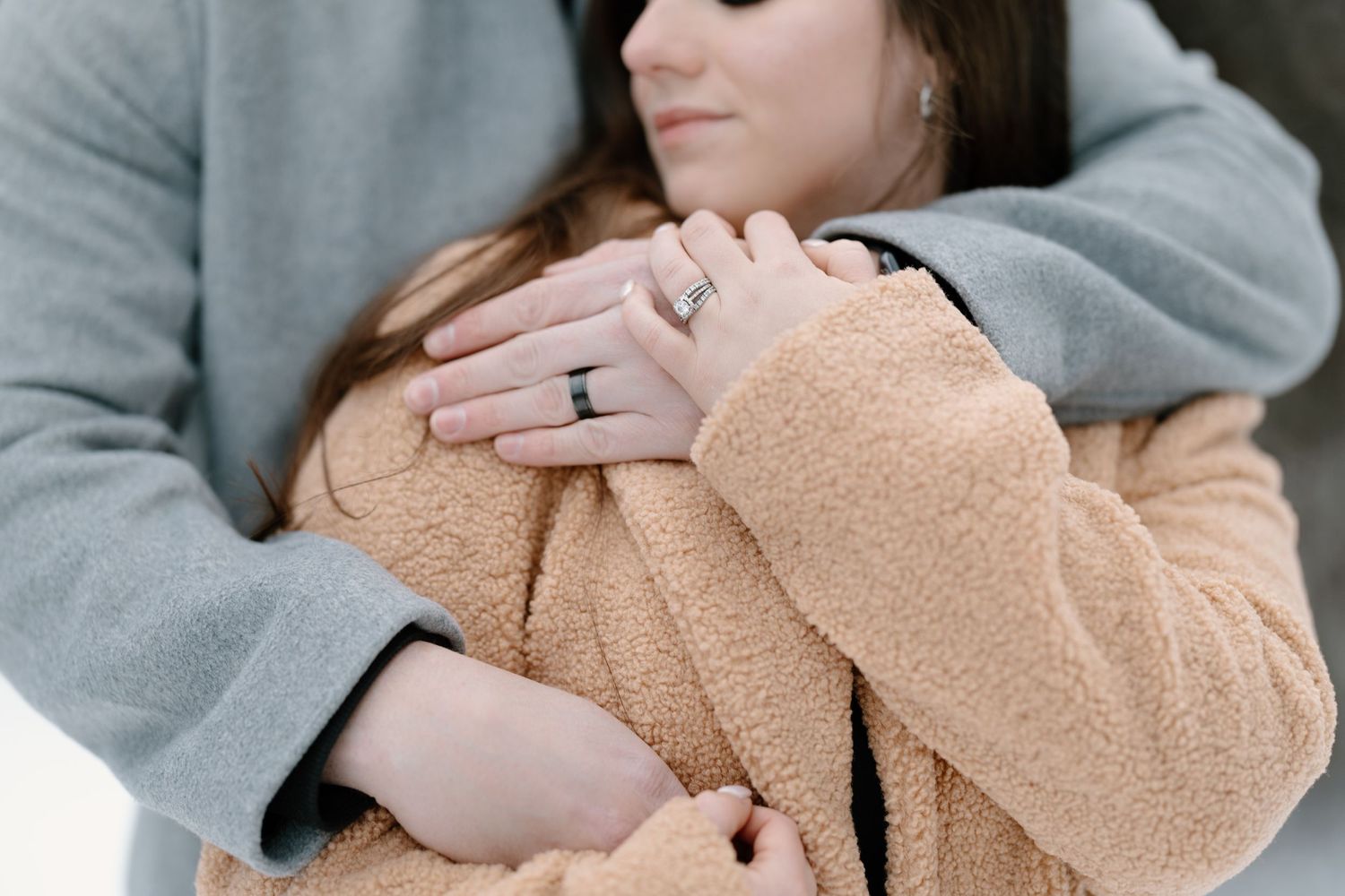 Close up of hands with engagement rings as couple embraces in cozy sweaters.