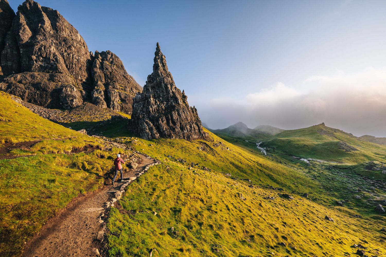 Dramatic rocky spire of Old Man of Storr rises above green hillsides on Isle of Skye, Scotland during golden hour.