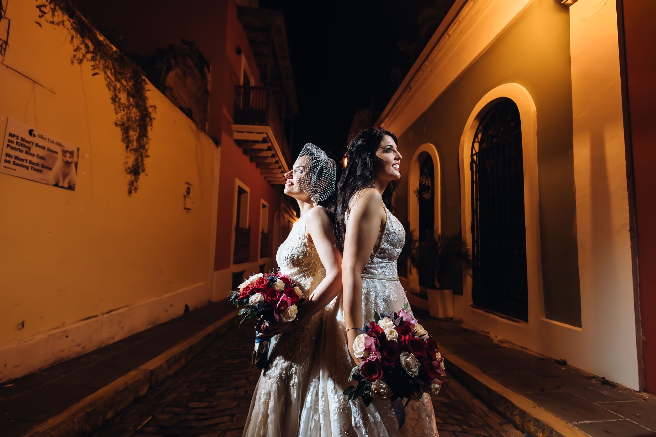 A group of people in white dresses walk through a dimly lit stone archway at night.