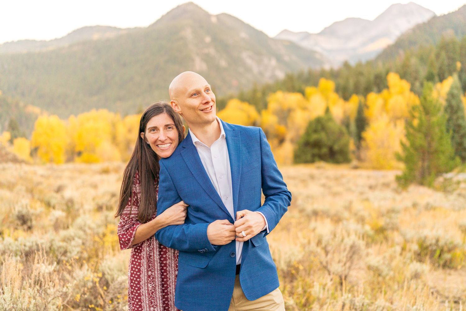 A couple embraces while laughing in front of mountain peaks with golden fall foliage at Granite Flat Campground, Utah.