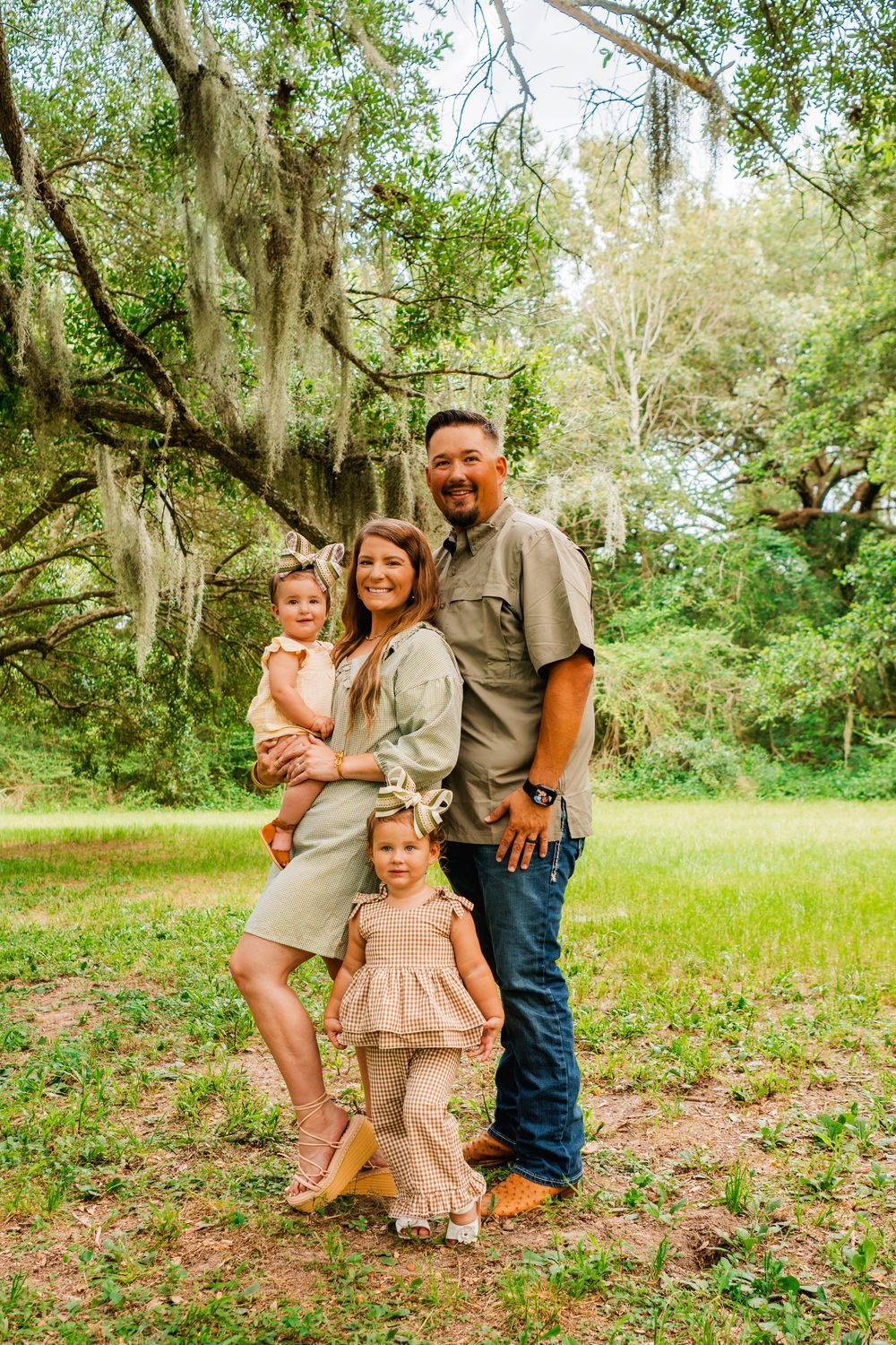 Family of four posing outdoors under a large oak tree with Spanish moss on a green lawn.
