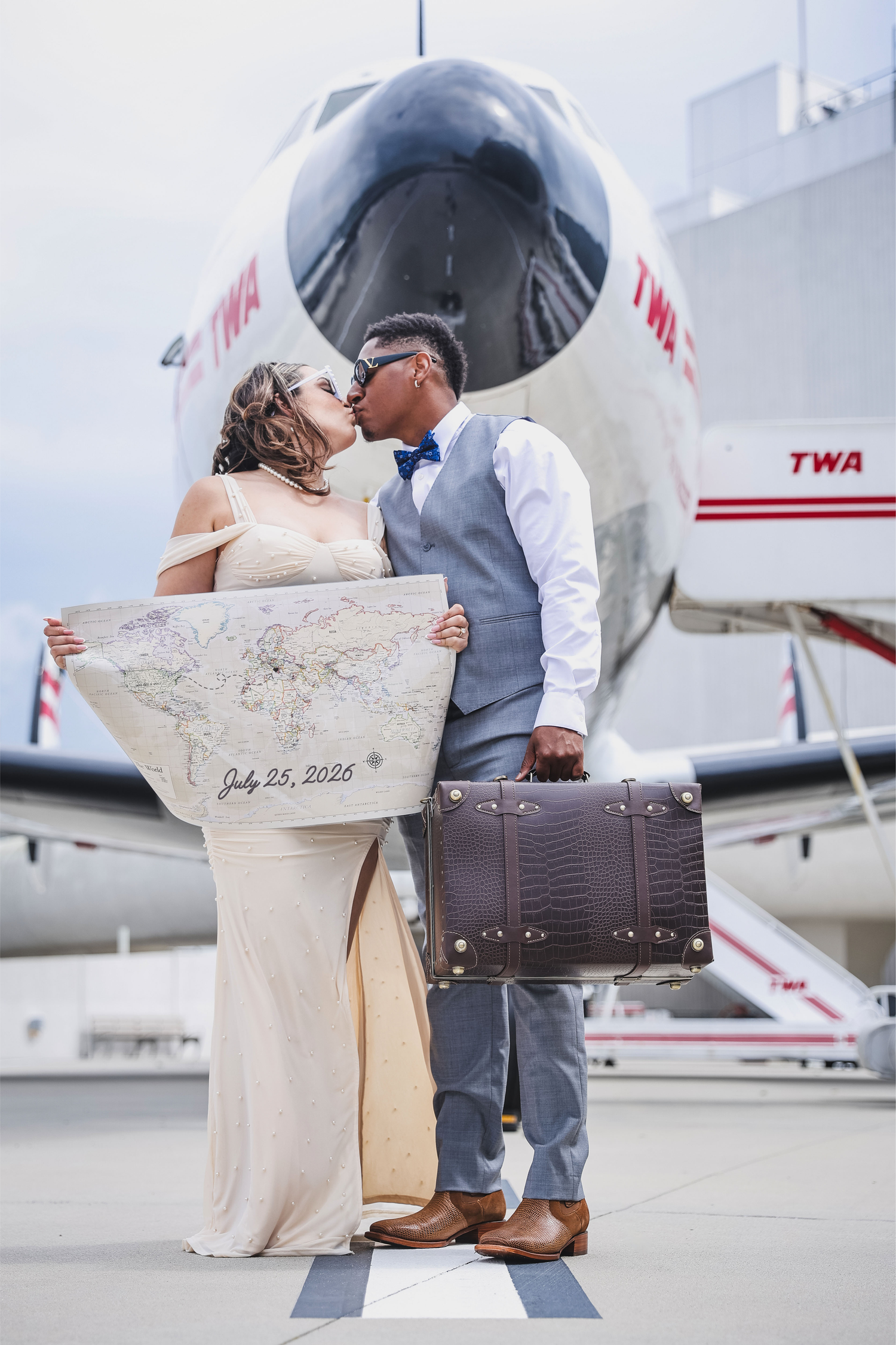 Romantic couple poses with vintage luggage by TWA airplane for wedding photos.