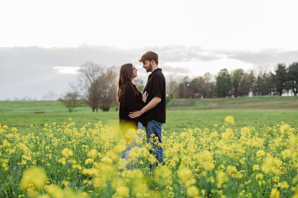 A couple embraces while standing in a vibrant yellow wildflower field on an overcast spring day.