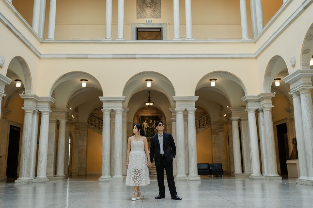 A grand interior hallway with white columns and arches features people gathered in formal attire for an event.