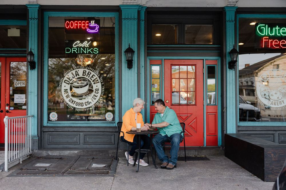 Two people sit at a small table outside a cafe with teal storefront and red door in downtown Portland.