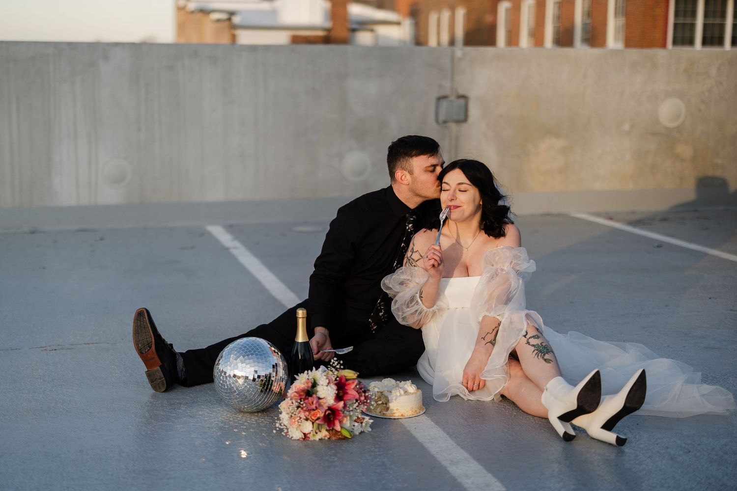 Couple sitting on concrete floor with disco ball and floral arrangement for romantic urban photoshoot.