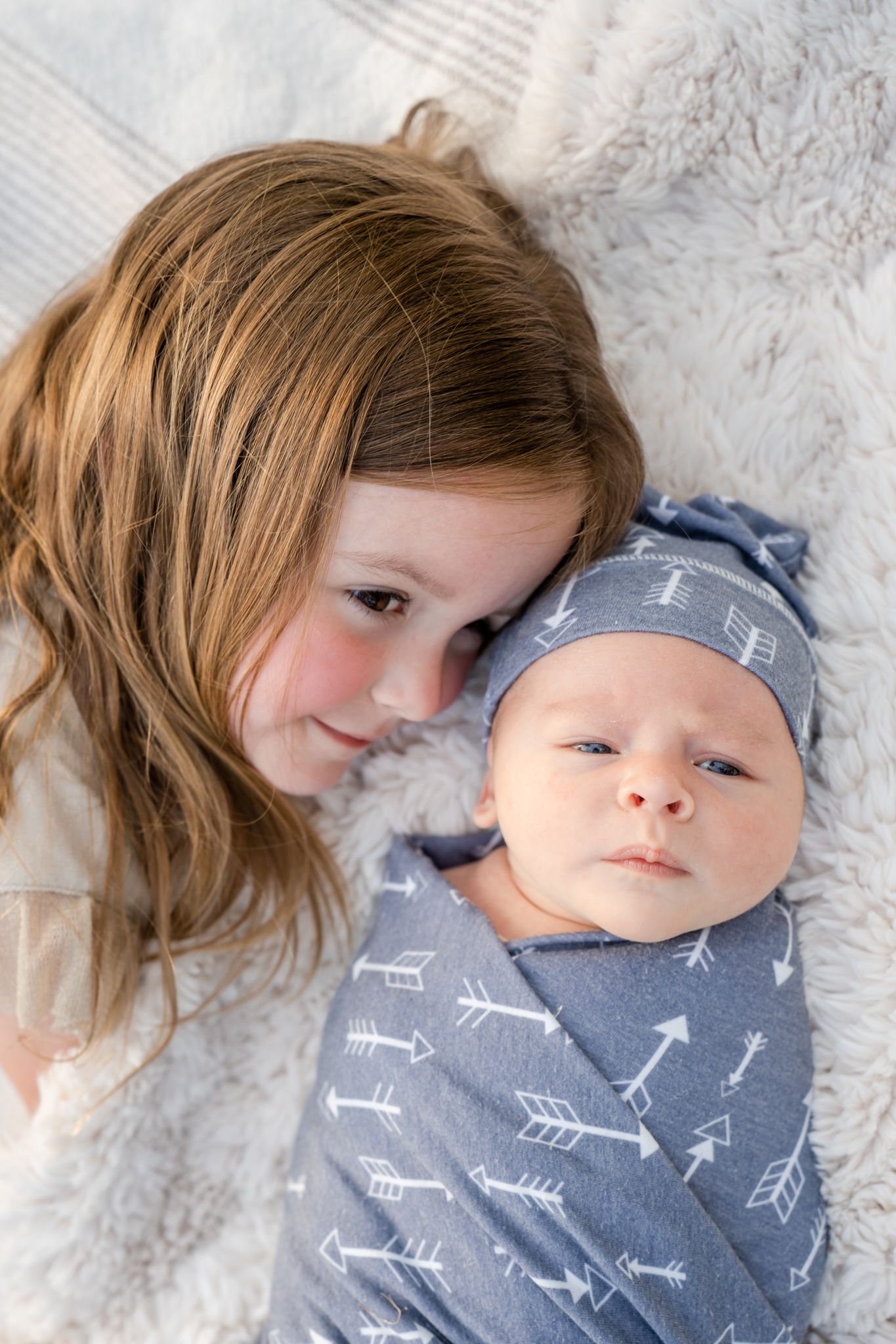 big sister snuggles by newborn brother on a white blanket