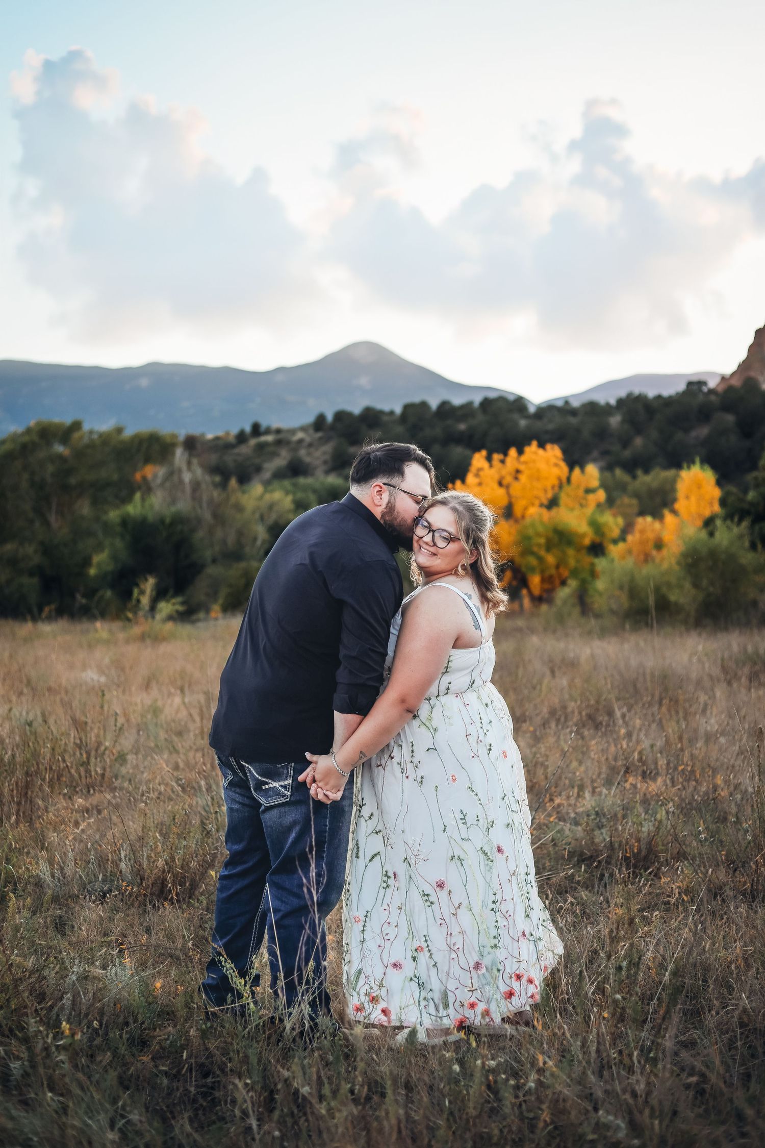 Couple embracing in golden field with mountains and autumn colors in background. Example of a wedding photography sessions