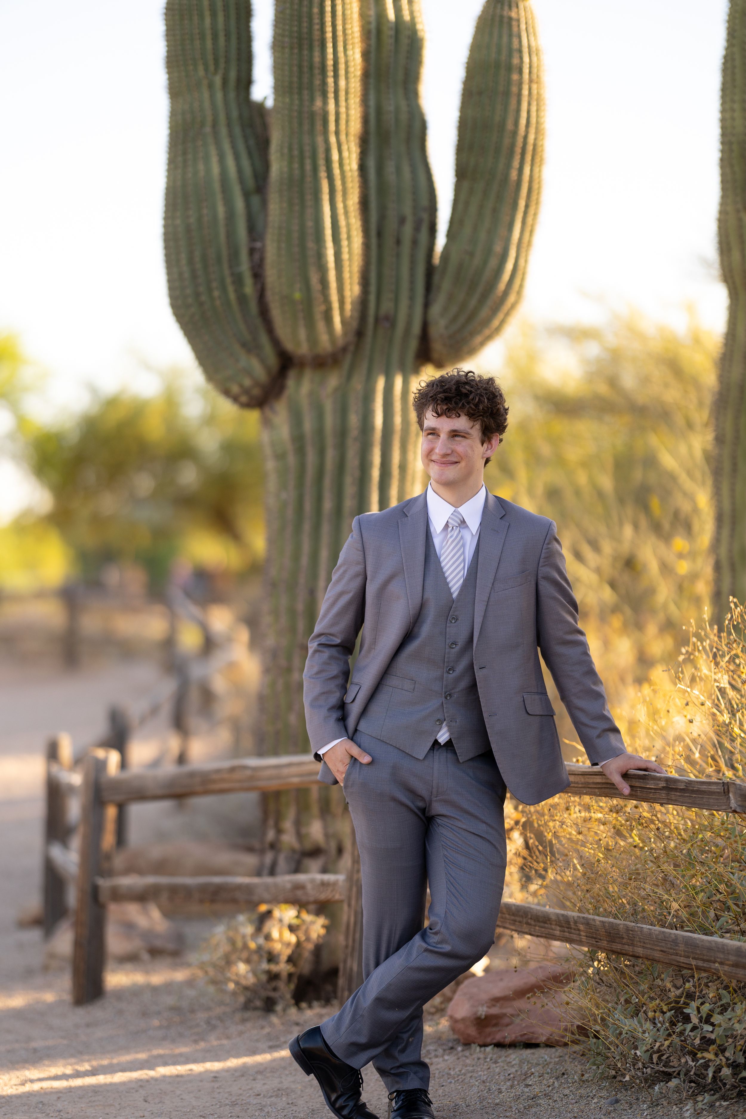 Person in gray suit poses casually against saguaro cactus backdrop at sunset.