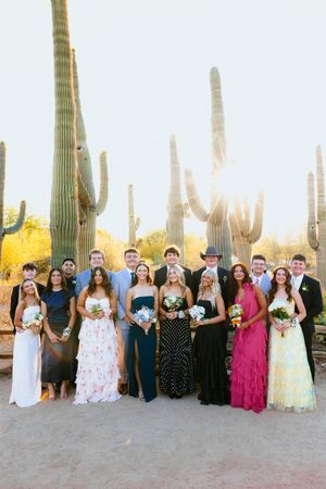 Wedding party posing in front of tall saguaro cacti in Arizona desert landscape, wearing colorful formal attire.