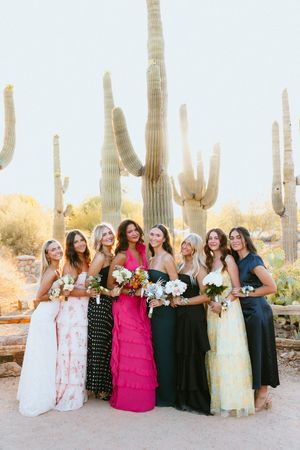 Eight bridesmaids in colorful mismatched gowns pose together holding bouquets in front of saguaro cacti.