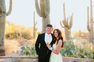 Couple in formal attire posing before tall saguaro cacti in Arizona desert landscape at golden hour.