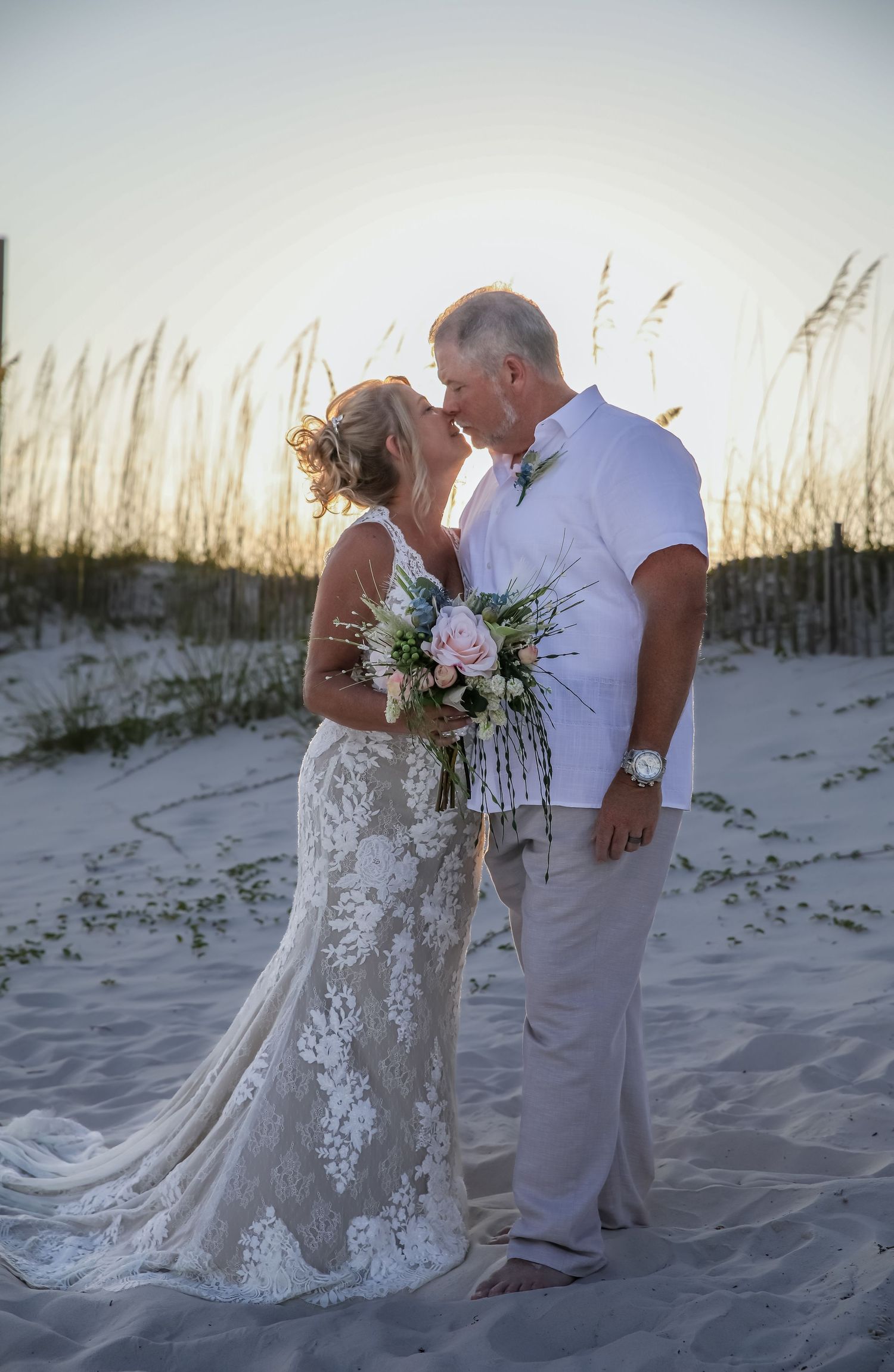 Intimate wedding portrait among sand dunes and sea oats during golden hour.