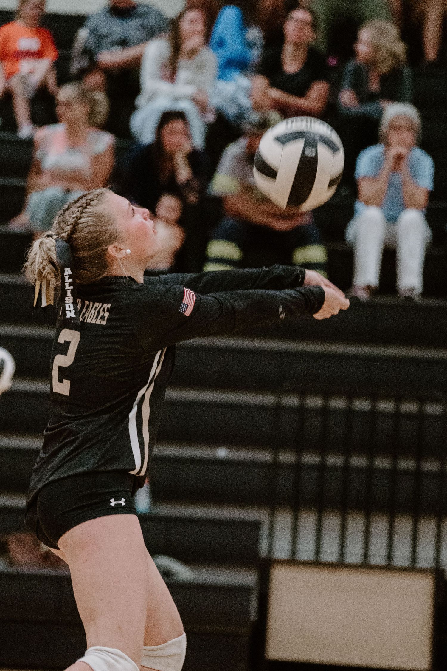 Volleyball players in black uniforms jumping to block at the net during an indoor match.