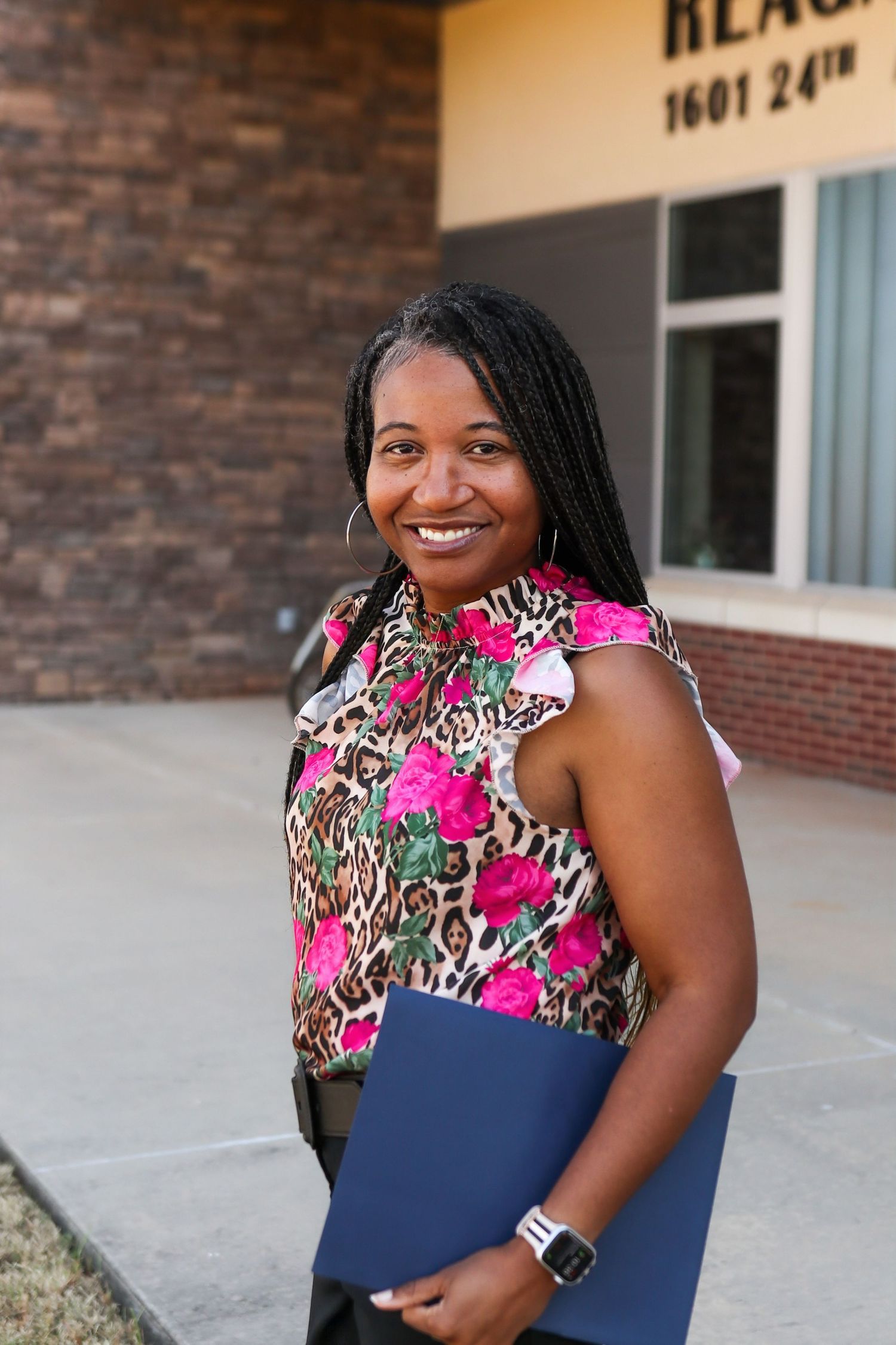 Professional portrait of a woman in business attire standing against an urban building backdrop.