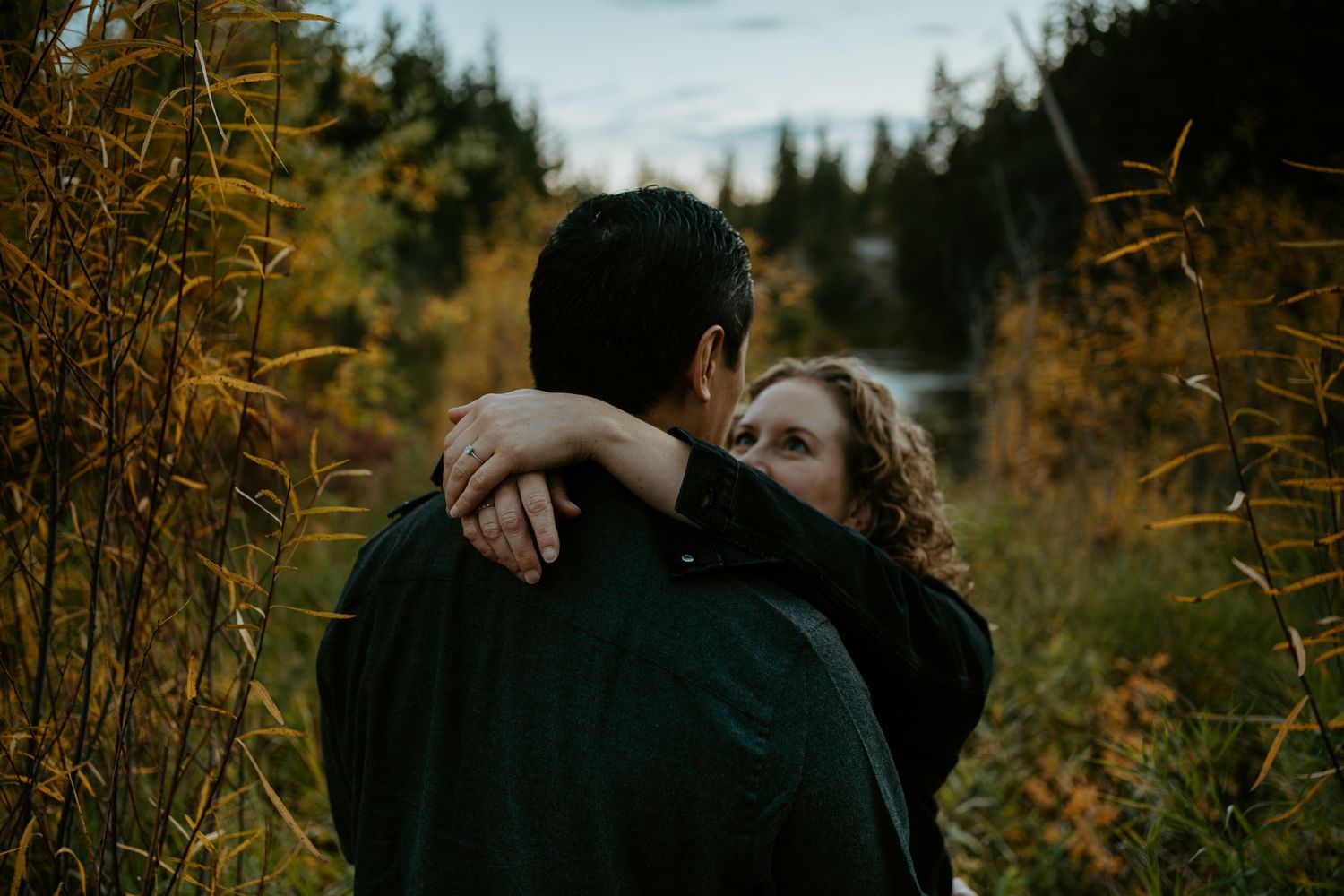 Two people embrace in a tender moment among golden autumn foliage in a forest setting in Alberta, Canada.