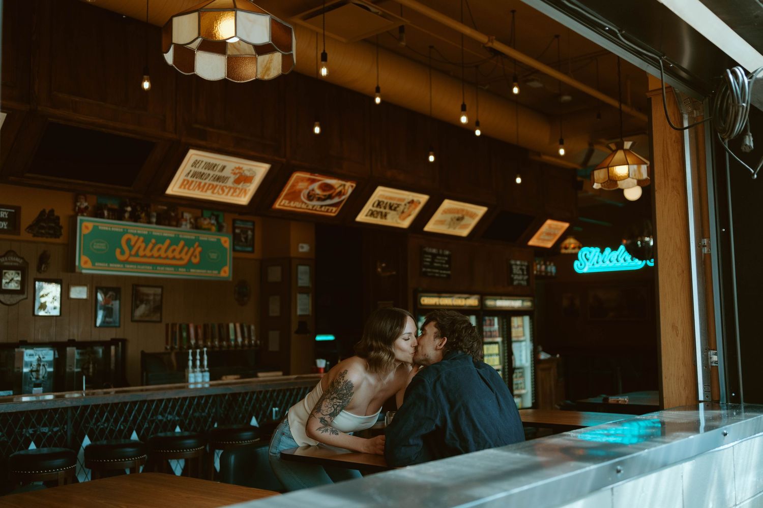 Couple sharing a romantic kiss at a cozy bar counter inside a warmly lit Sliddys restaurant.