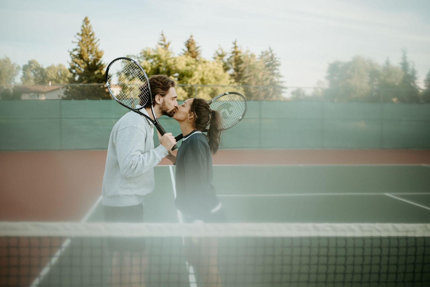 A couple share a romantic moment together on an outdoor tennis court during golden hour.