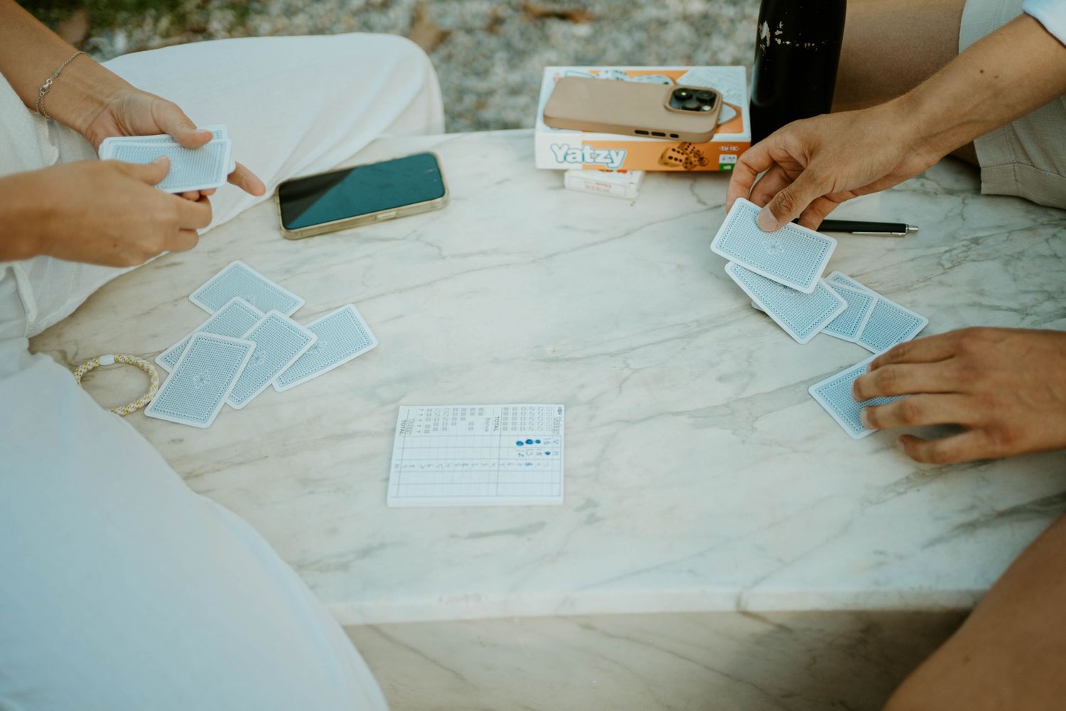 Overhead view of hands playing cards on a white tablecloth.