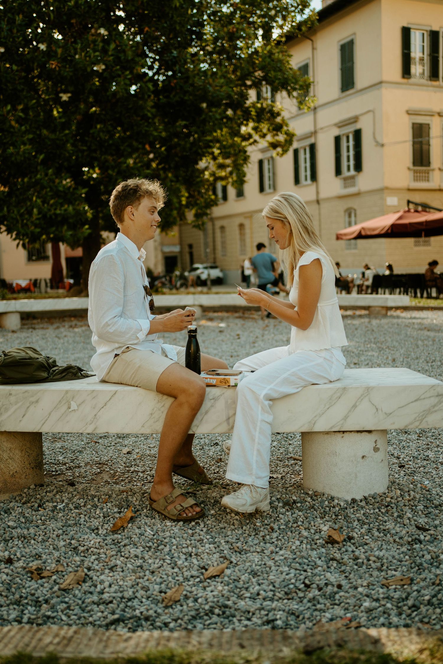 Two people enjoying drinks and conversation on a stone bench in an Italian courtyard.