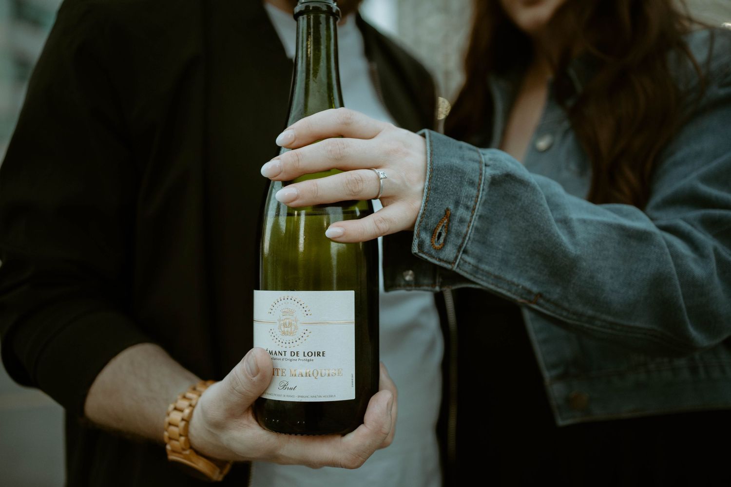 A person holds a glass bottle of wine against a dark background with blurred lighting effects.