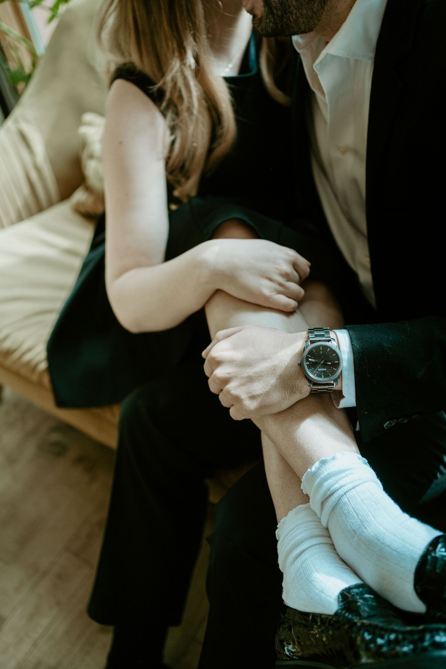 Close up of person wearing silver watch with white socks as they sit, showing intimate moment on hardwood floor.