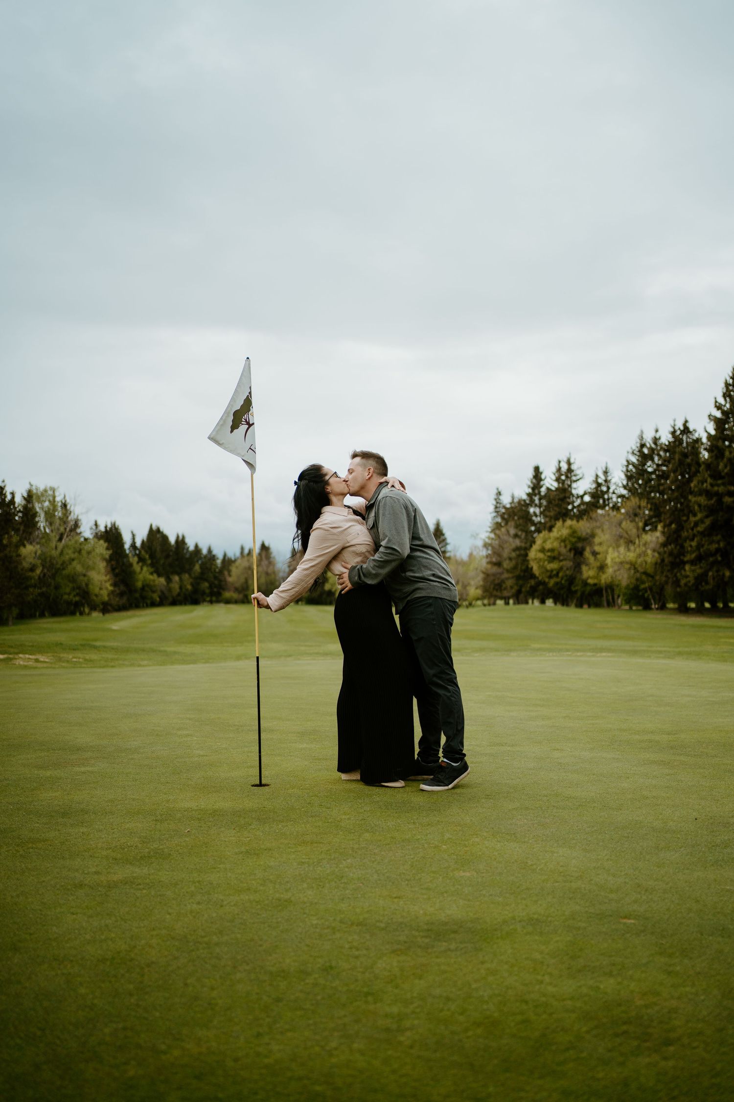 A couple sharing a tender moment on a golf course green next to a flag pole.