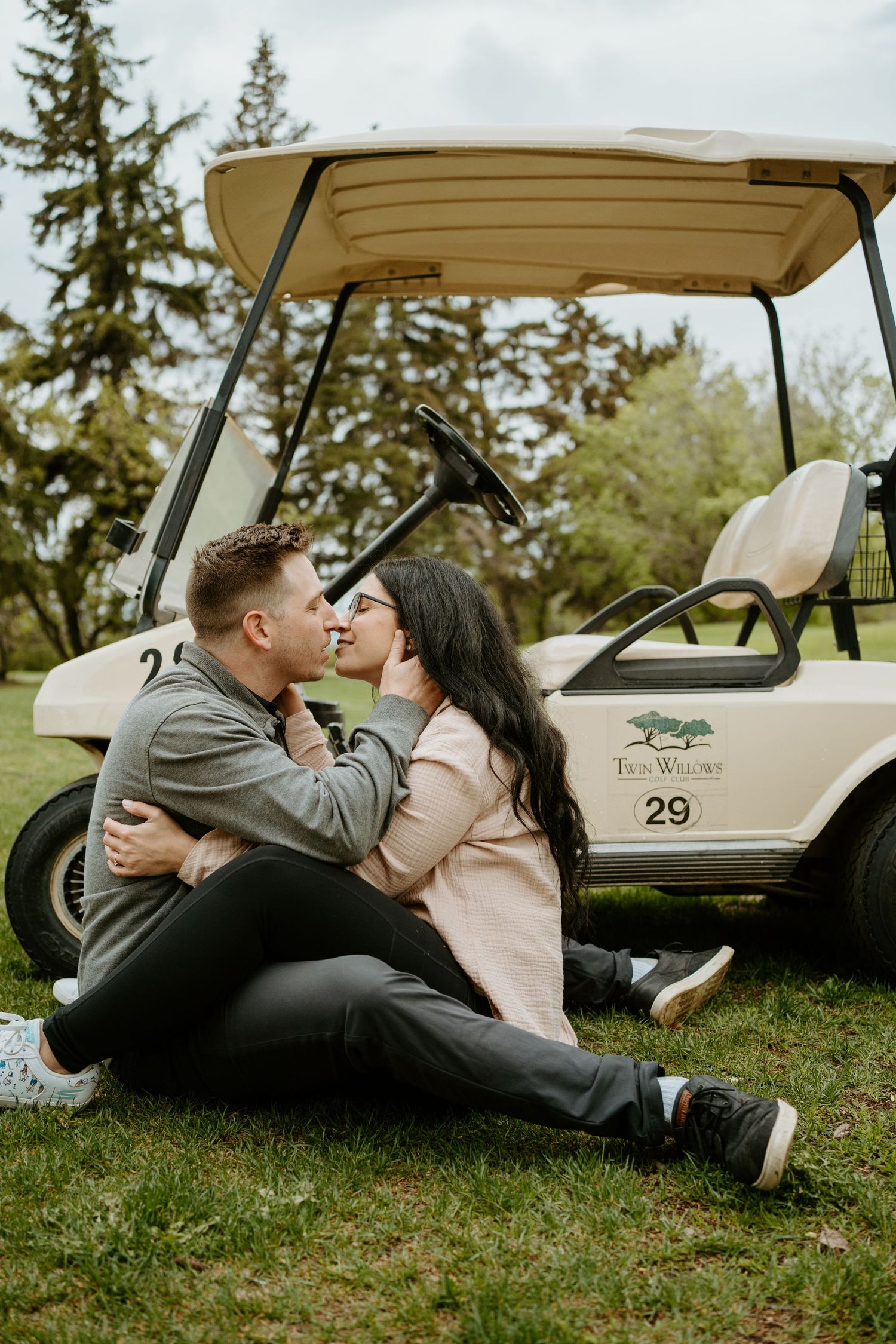 A romantic couple embraces near a golf cart on a grassy lawn.