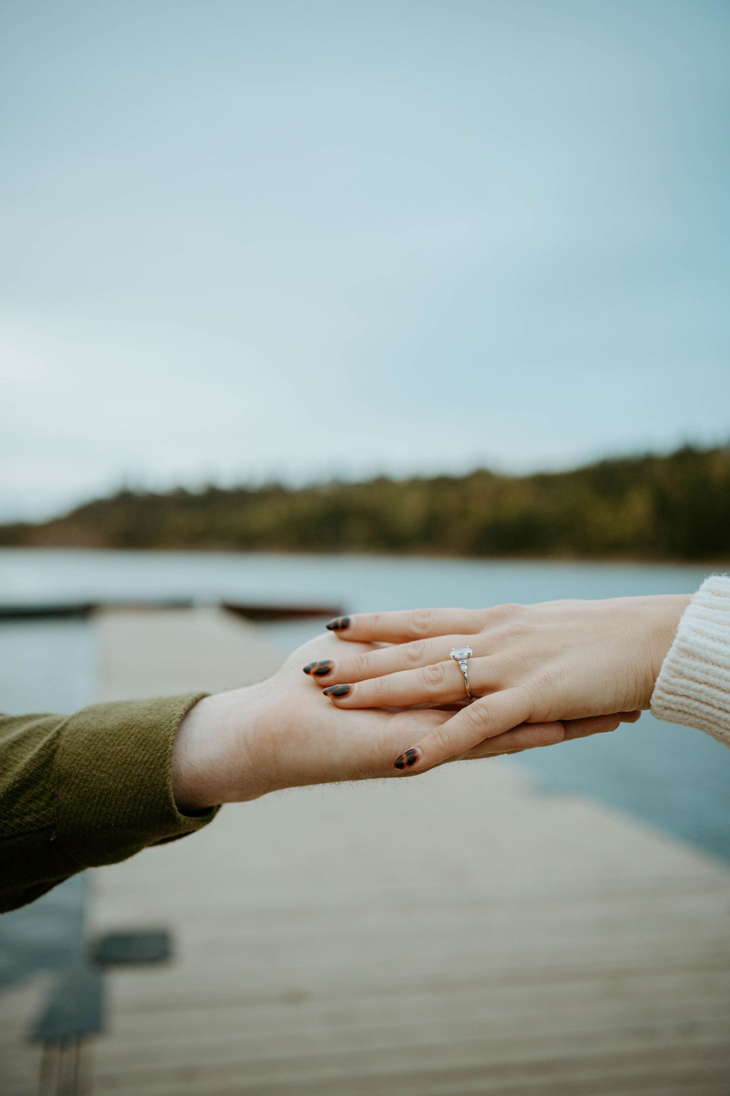 Two hands reaching towards each other against a blurred waterfront background in soft muted tones.