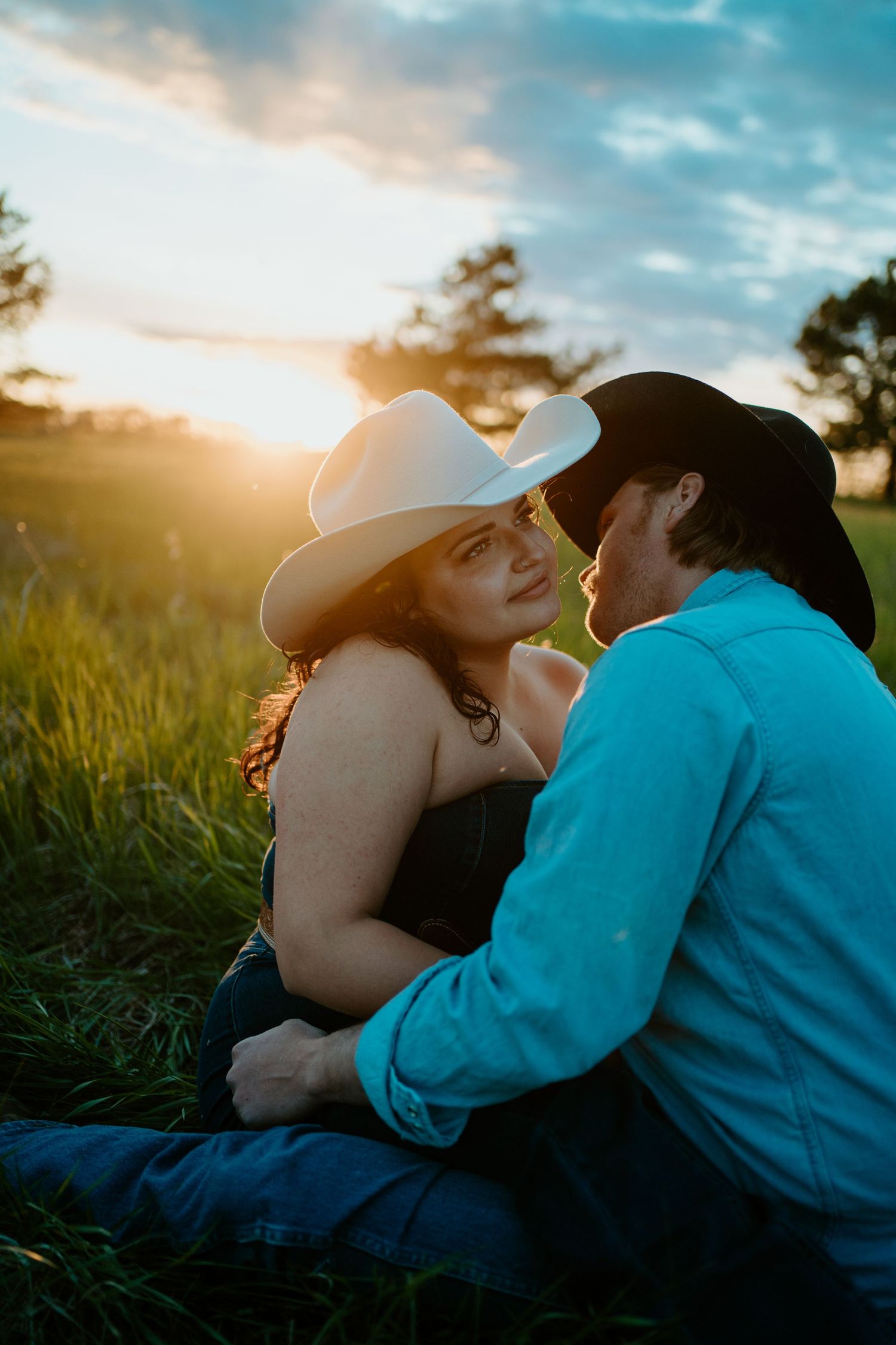 A romantic couple sharing an intimate moment in a grassy field during golden hour sunset.